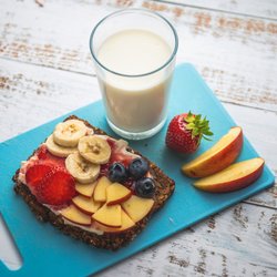 Frühstücksbrett mit einem Glas Milch und einem mit Obstscheiben belegtem Brot