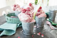 Drei Becher Frozen Yoghurt, dekoriert mit Himbeeren auf einem Tisch