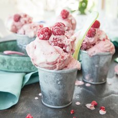 Drei Becher Frozen Yoghurt, dekoriert mit Himbeeren auf einem Tisch
