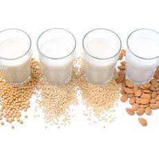 Vier Gläser mit Pflanzendrinks und deren Ausgangsprodukte